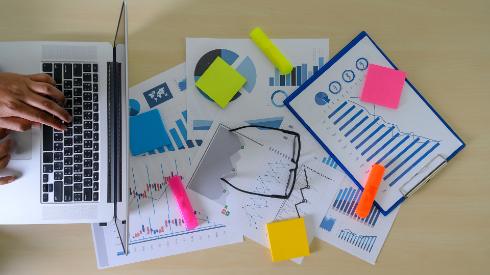 A businessperson working on a advertising campaign, with a laptop, papers and sticky notes on their desk