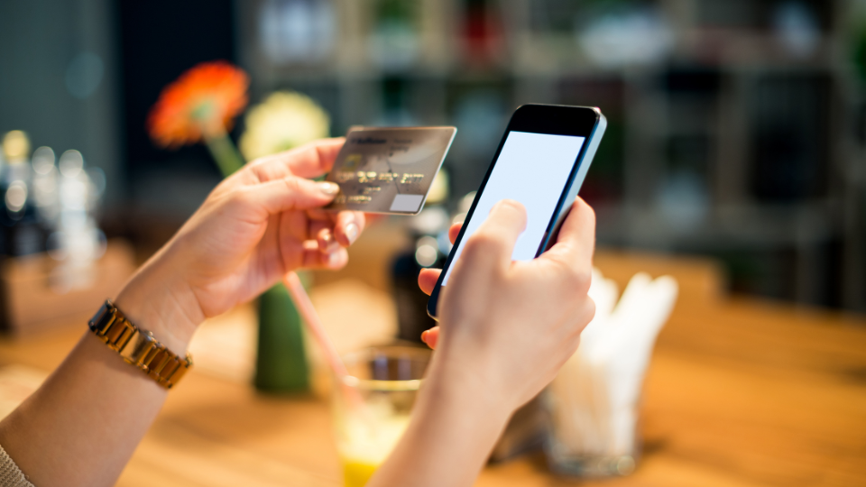 A person making a purchase on their cell phone while holding a credit card in their hand