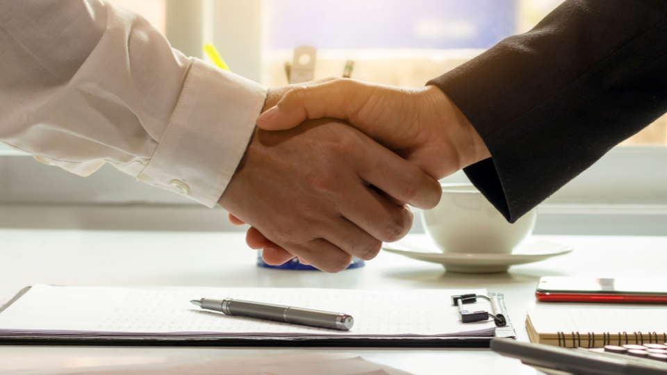 Two businesspeople shaking hands over a desk for brand approval