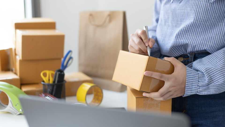 A person surrounded by boxes, writing on a package.
