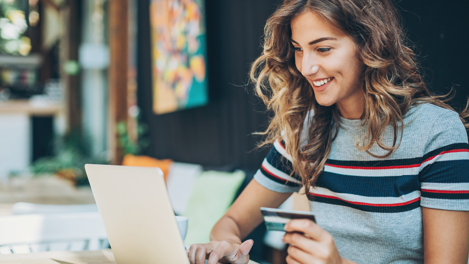 A person smiling using a laptop and credit card at a coffee shop