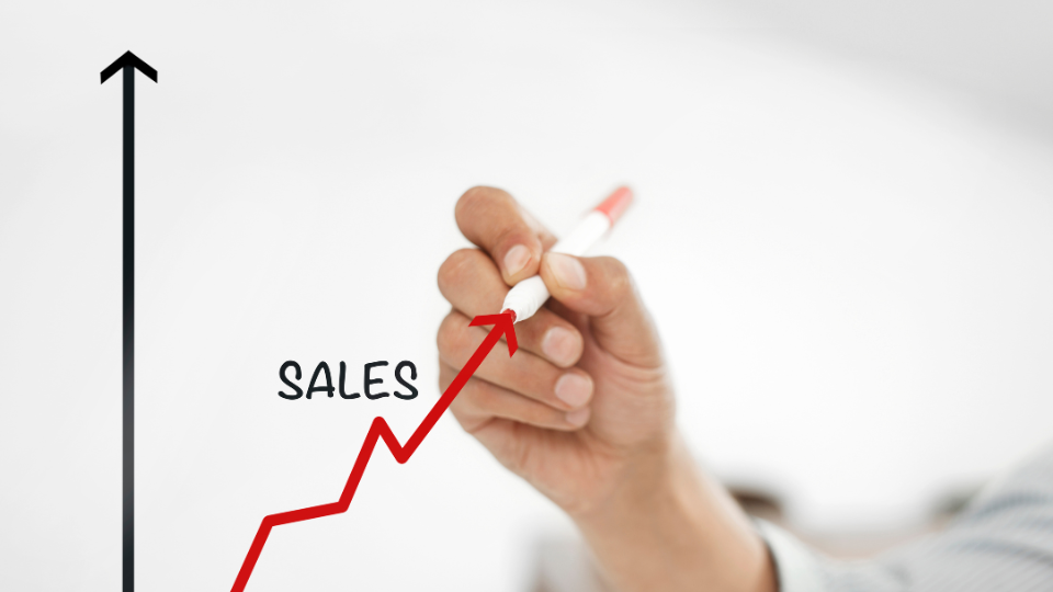 A person drawing a sales graph on a whiteboard with an upward-pointing arrow to indicate growth