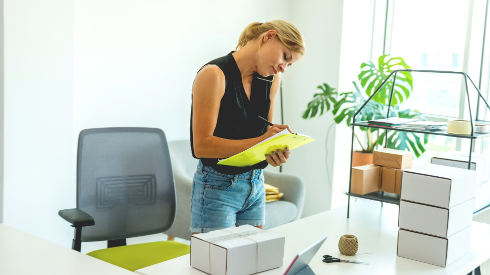 A person at their office desk, taking notes in a notepad while speaking on the phone with a supplier