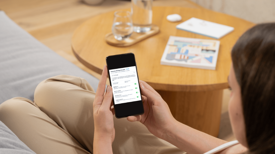 A person sitting on a couch, using their phone with the Informed Repricer Interactive Strategy Simulator displayed on the screen