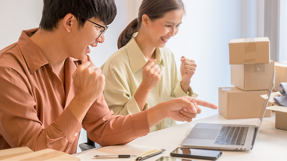 Two business people looking at their computer happily, with boxes in the background