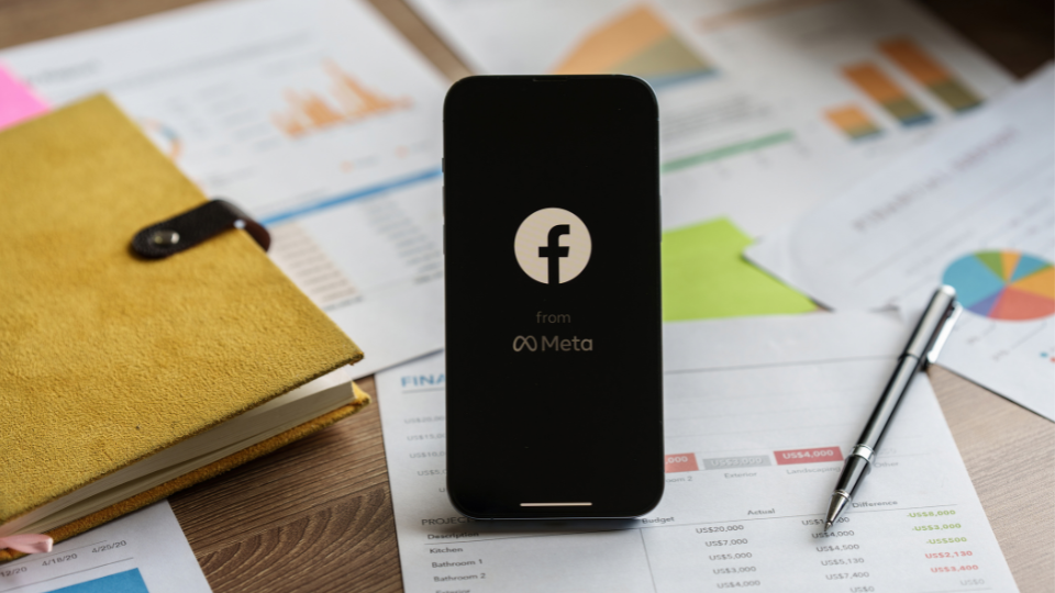 A phone sitting on an office desk, open to Facebook