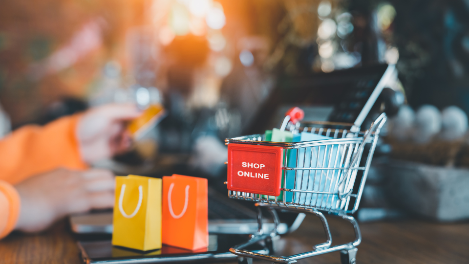 A mini shopping card on a desk, next to two mini shopping bags