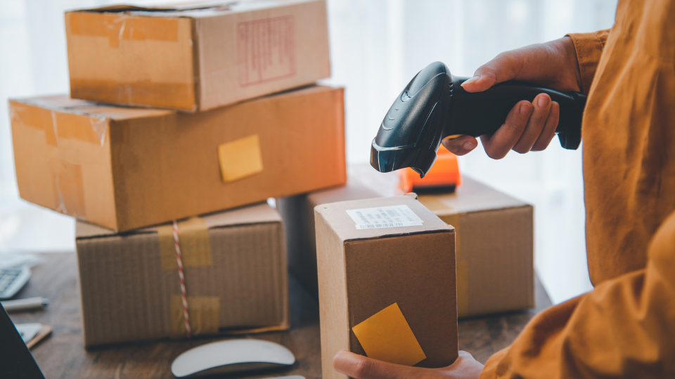 A person scanning a box in an office surrounded by packages
