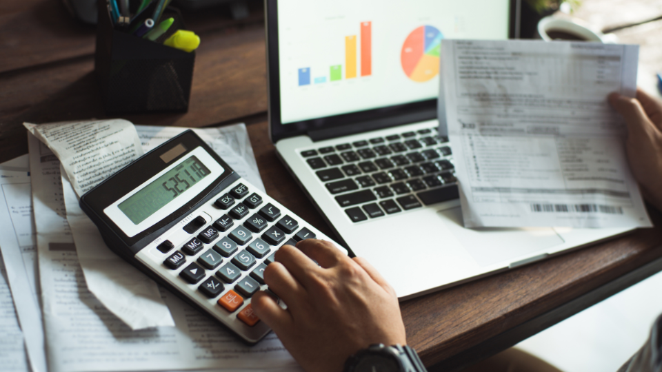 A person using a calculator on a desk to determine total costs