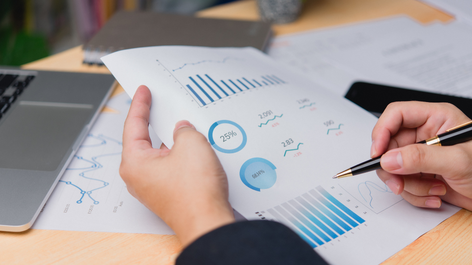 A person holding a pen and analyzing ad metrics on a piece of paper