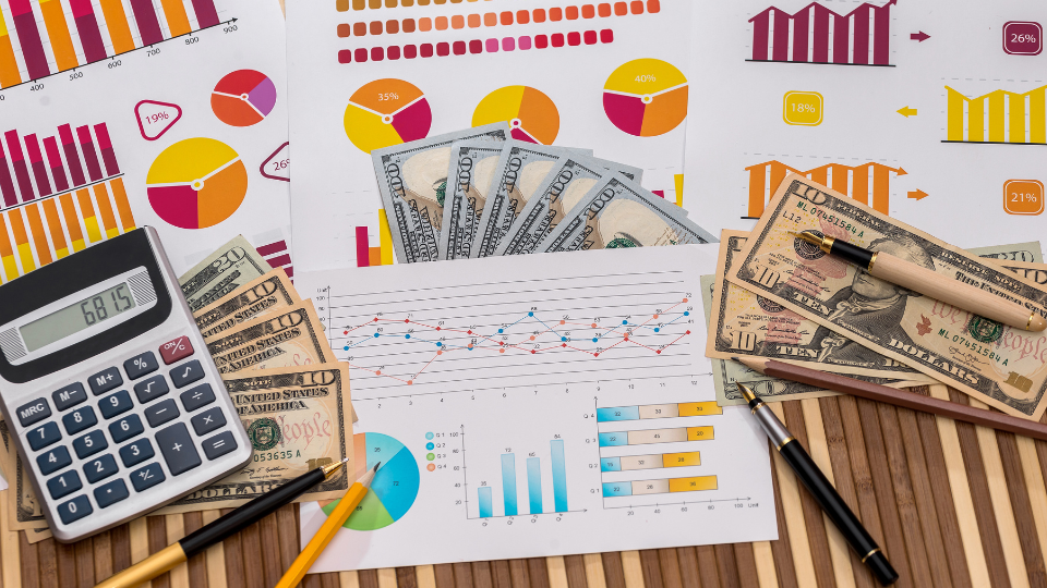 A close-up image of a desk with pricing strategy materials, including a graph, USD bills, a calculator, and pens
