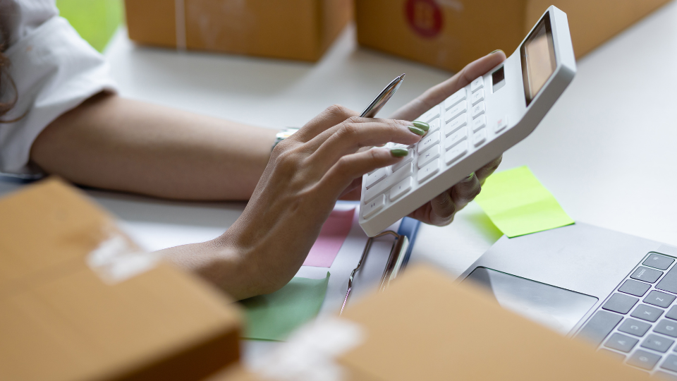 A person using a calculator on a desk with boxes around them
