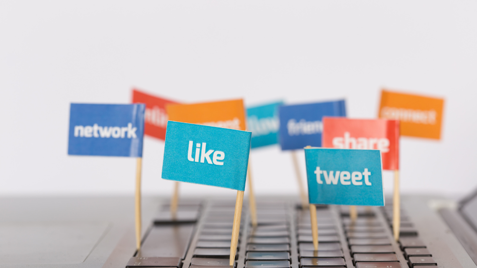 Small flags coming out of a laptop keyboard with social media themed words like “tweet” and “share”