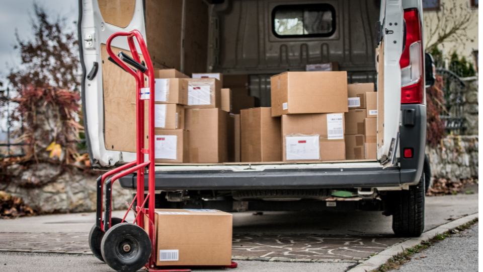 An open van with packages inside, and a hand cart sitting near the trunk