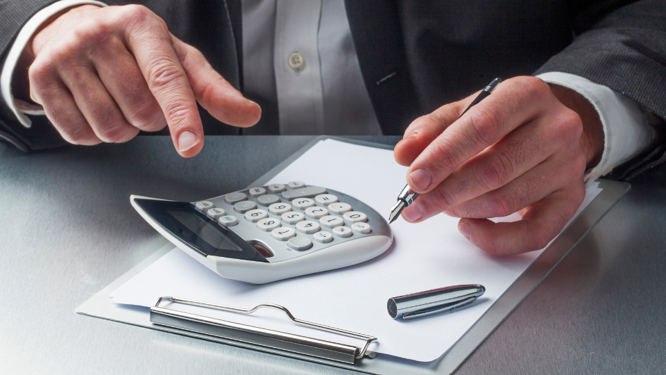 A person in a suit at a desk with a calculator, pen, and clipboard