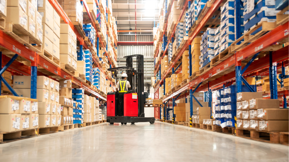 A forklife operator working on fulfilling orders in a warehouse with rows of pallets and boxes